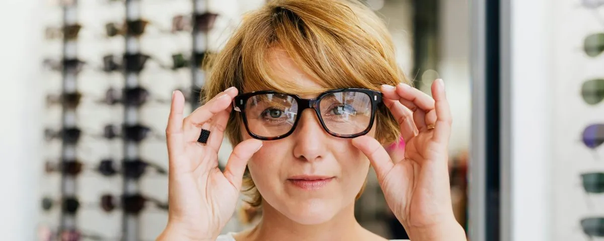 A woman facing the camera tries on a pair of glasses at the optometrist's.