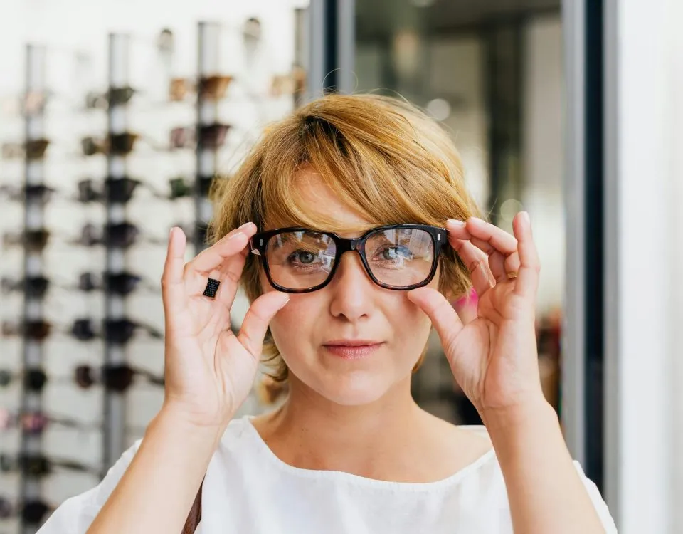 A woman facing the camera tries on a pair of glasses at the optometrist's.