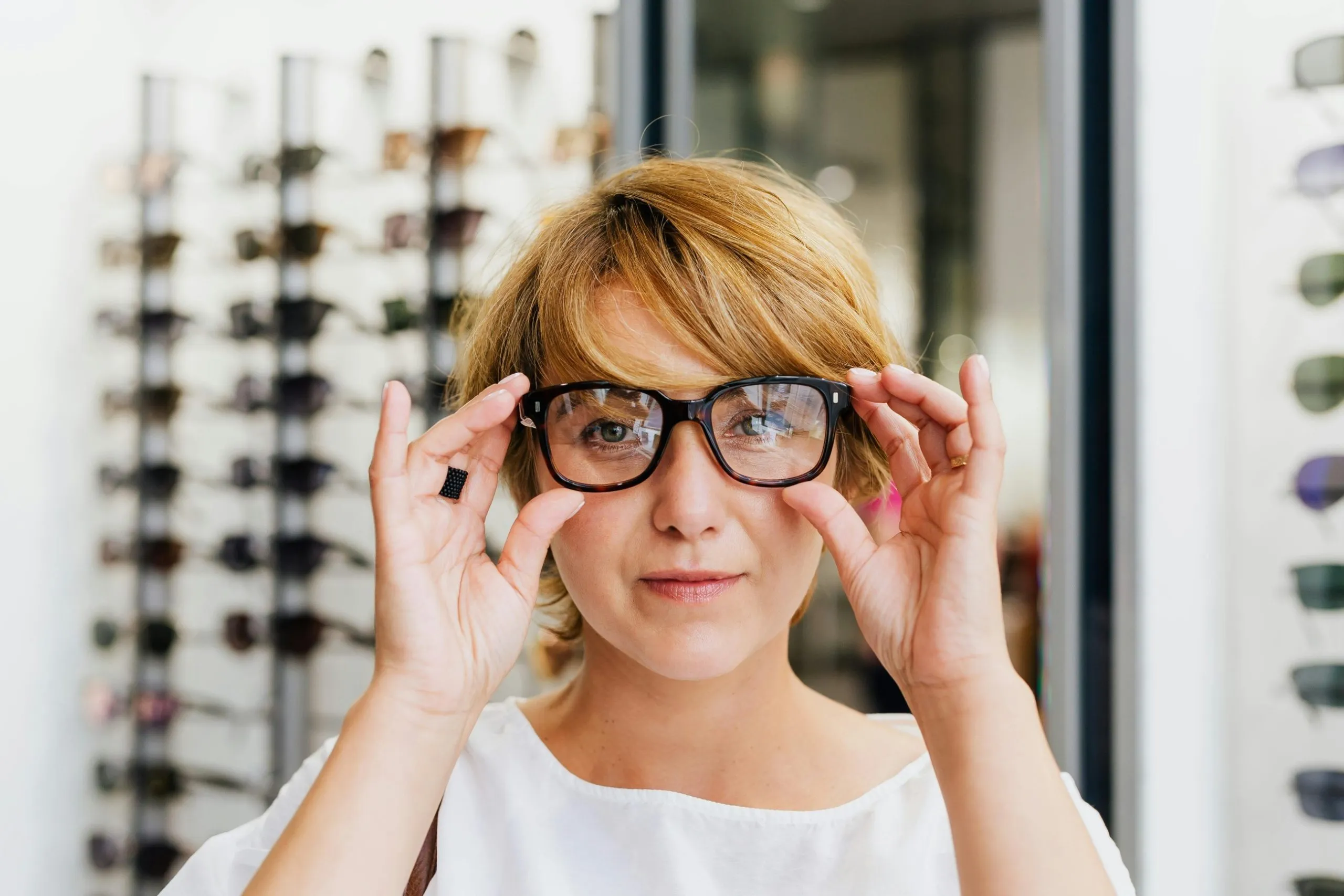 A woman facing the camera tries on a pair of glasses at the optometrist's.