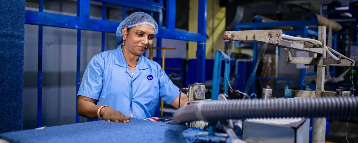 An Indian woman wears a blue uniform and hairnet and operates a machine in a factory.