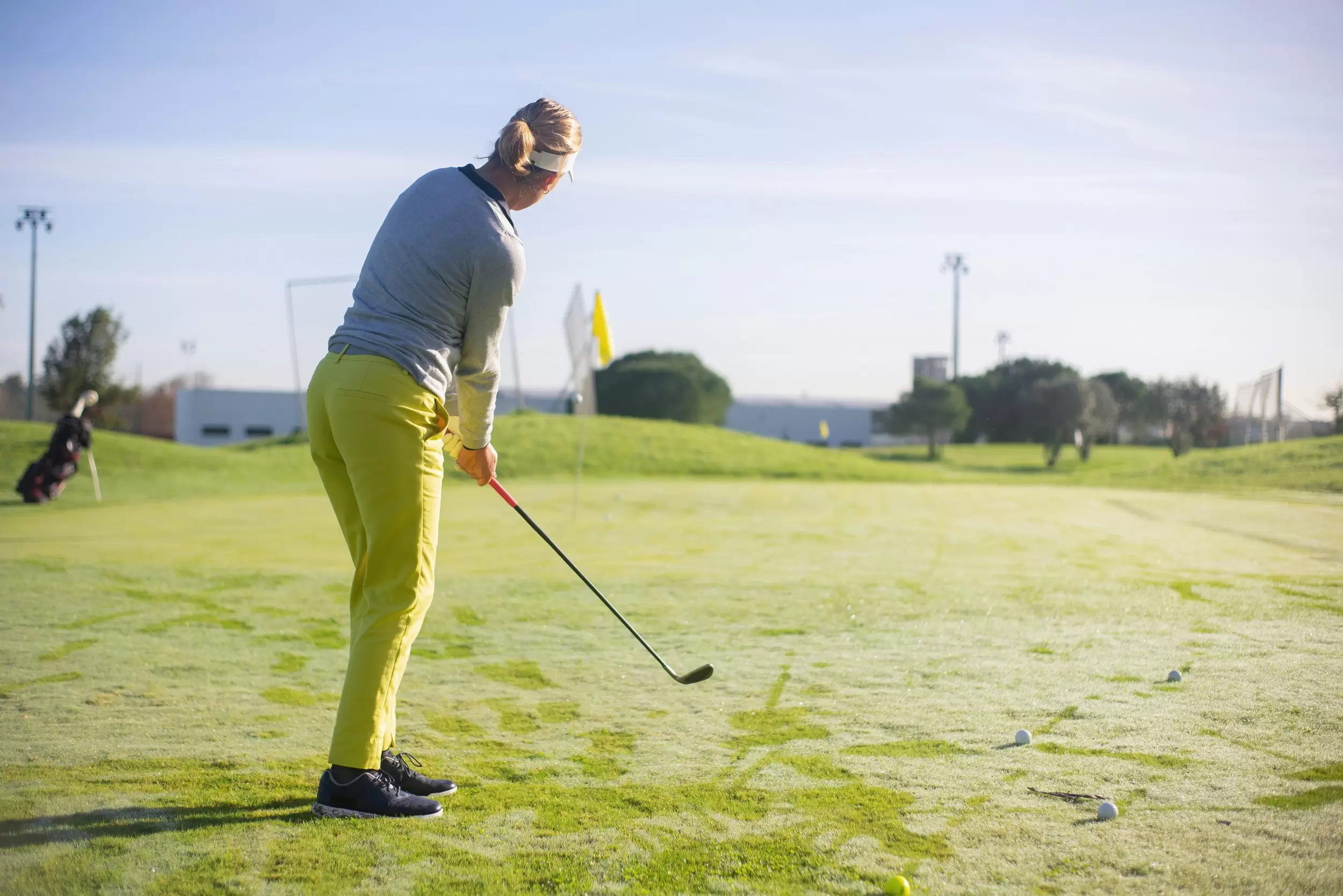 A back and side view of a woman standing on a golf green, looking into the distance preparing for her next shot.
