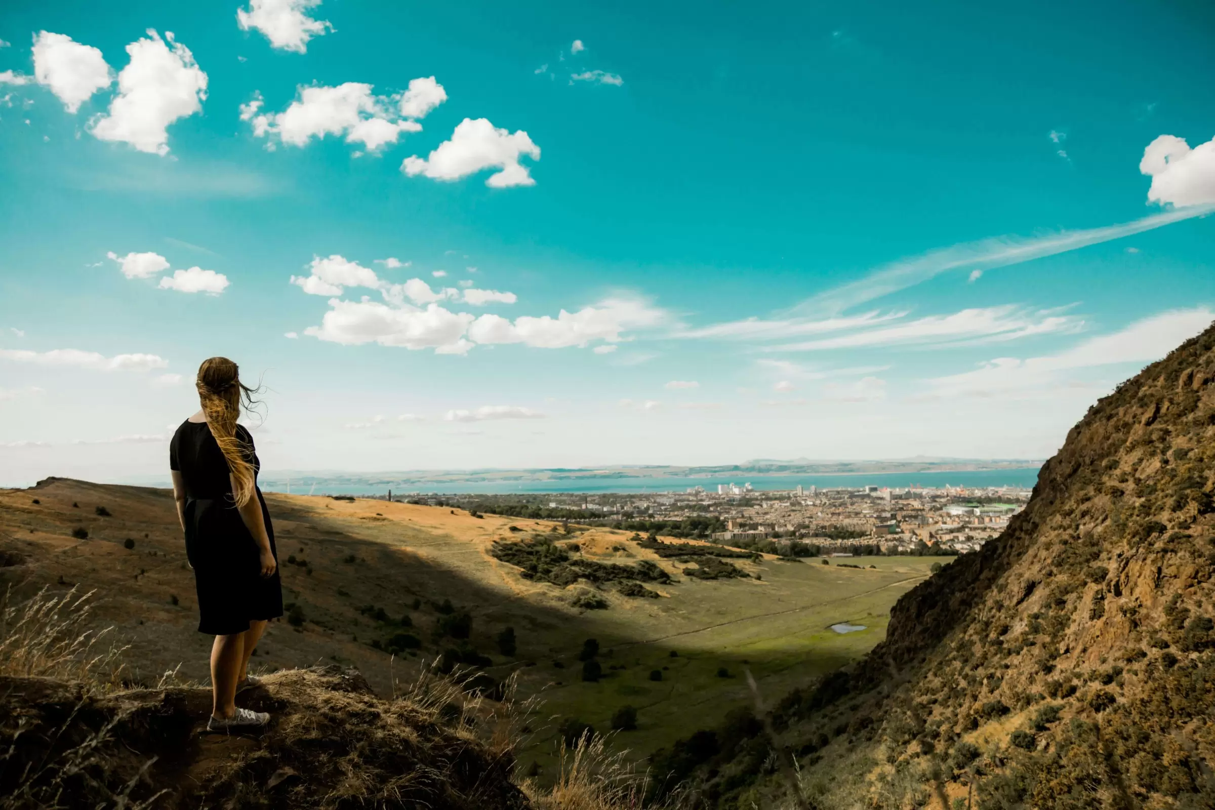Woman with long blond hair stands on a mountain overlooking Plainfield in Edinburgh, Scotland.